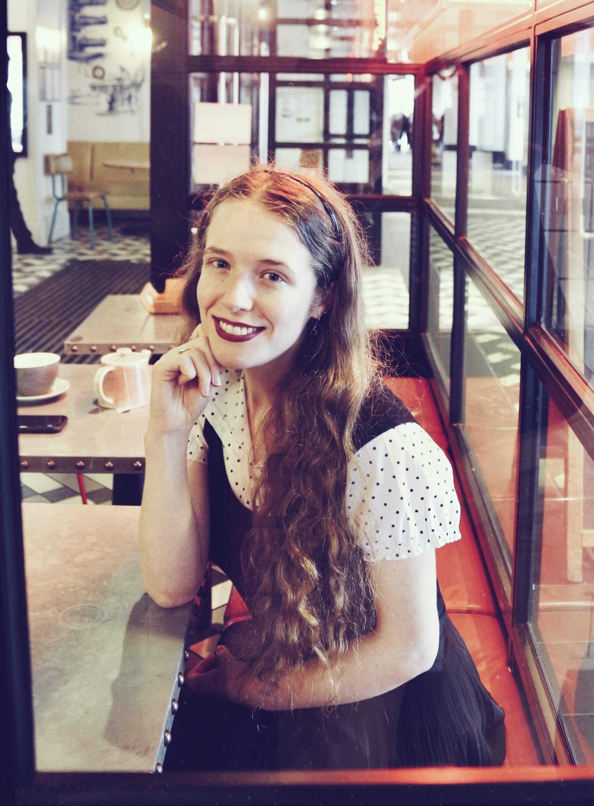 Young white woman with long red hair sitting on a bench in a modern cafe, looking up at the camera