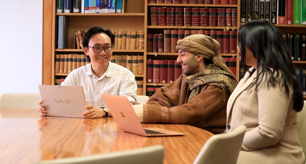 Three students at a table in the library laughing together whilst having a discussion.