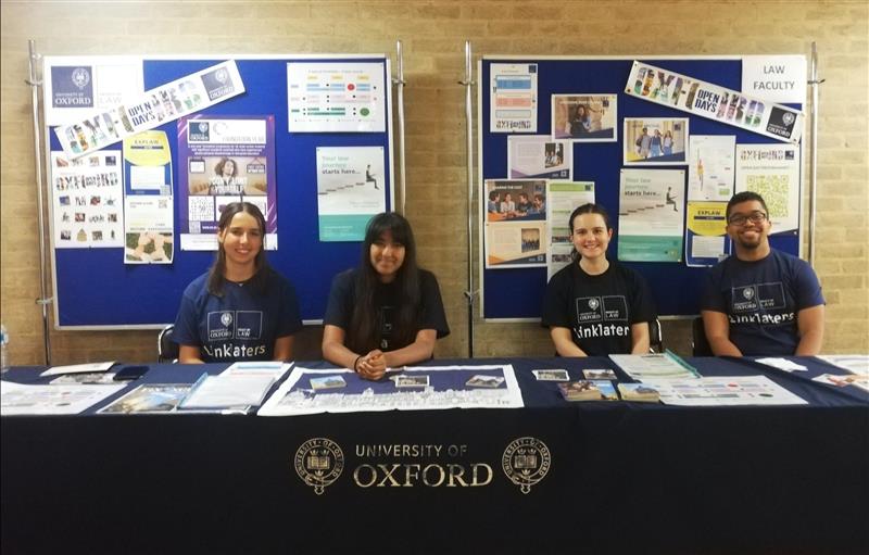 4 students sat down at a table advertising law at the University Open Day