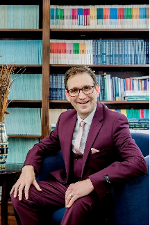 A picture of David Bilchitz seated in front of a shelf full of books. Bilchitz is wearing a burgundy suit.