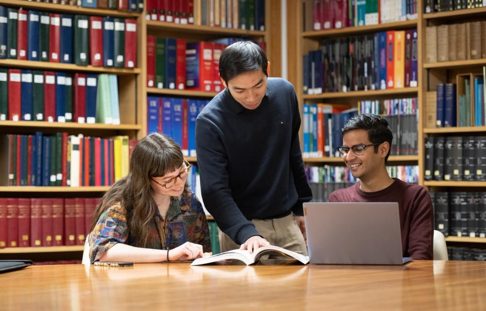 Three students in the library looking at a book