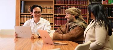 Three students at a table in the library laughing together whilst having a discussion.