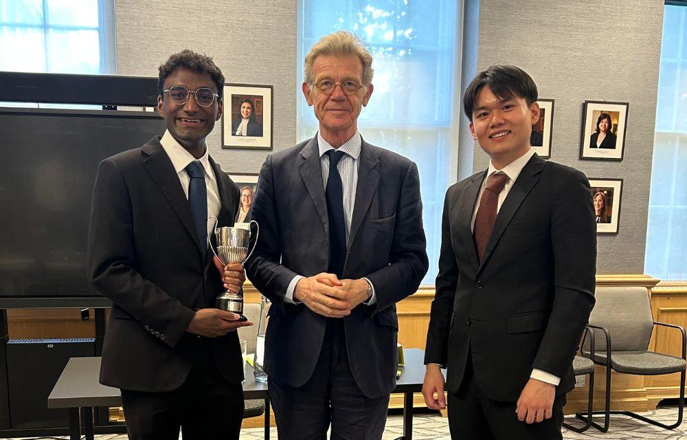 Oxford undergraduates Navin Sivakumar and Lukas Lim with the Kingsland Cup alongside the presiding judge Sir Keith Lindblom.