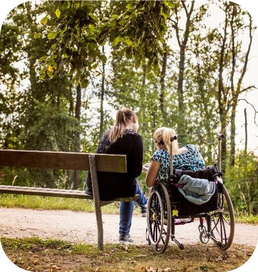 A woman on a park bench and another in a wheelchair chatting