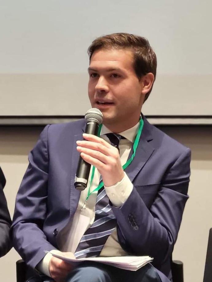 Looking sideways, formally dressed and speaking ino a mic