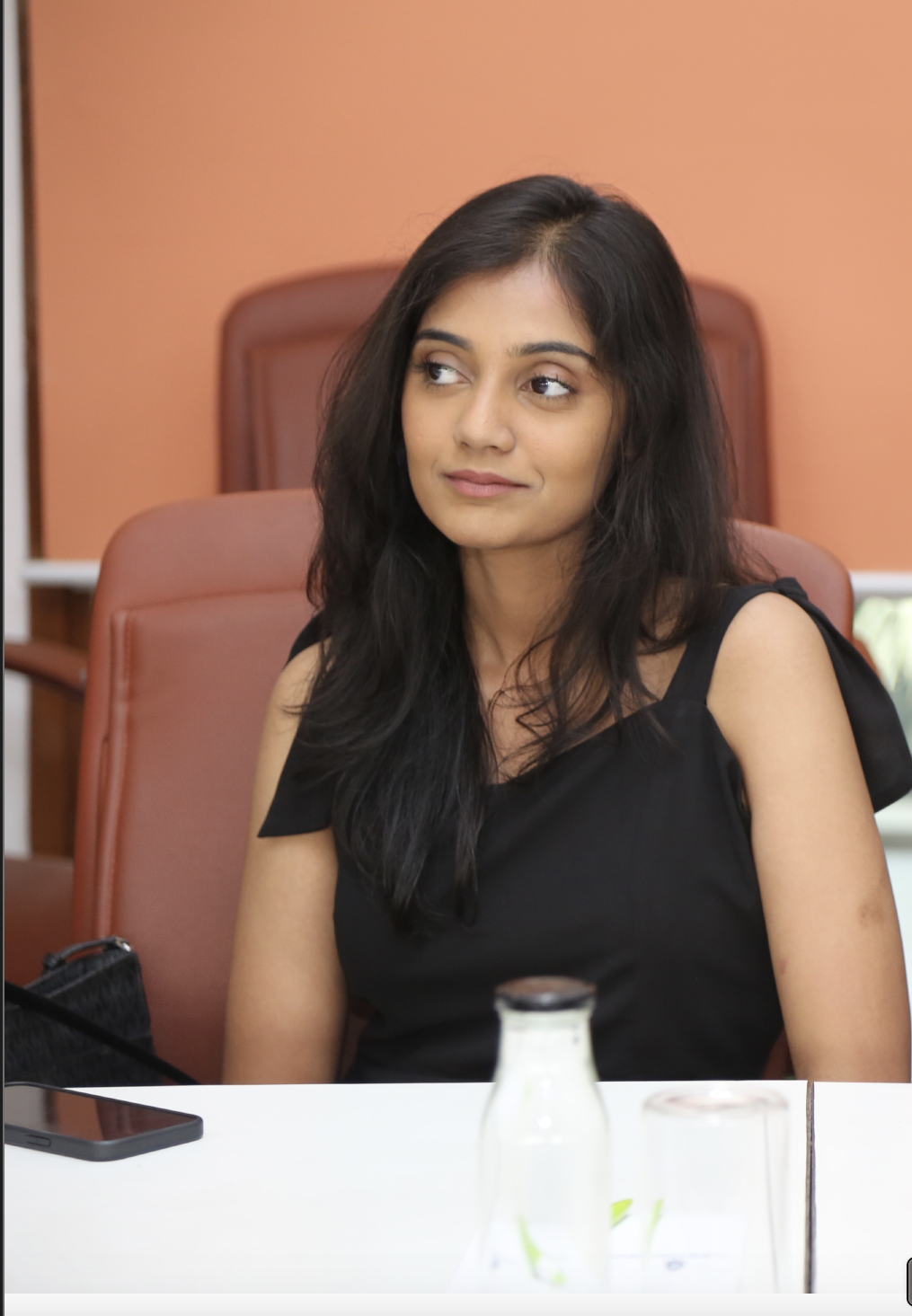 Looking sideways at the camera and wearing a black sleeveless dress.
