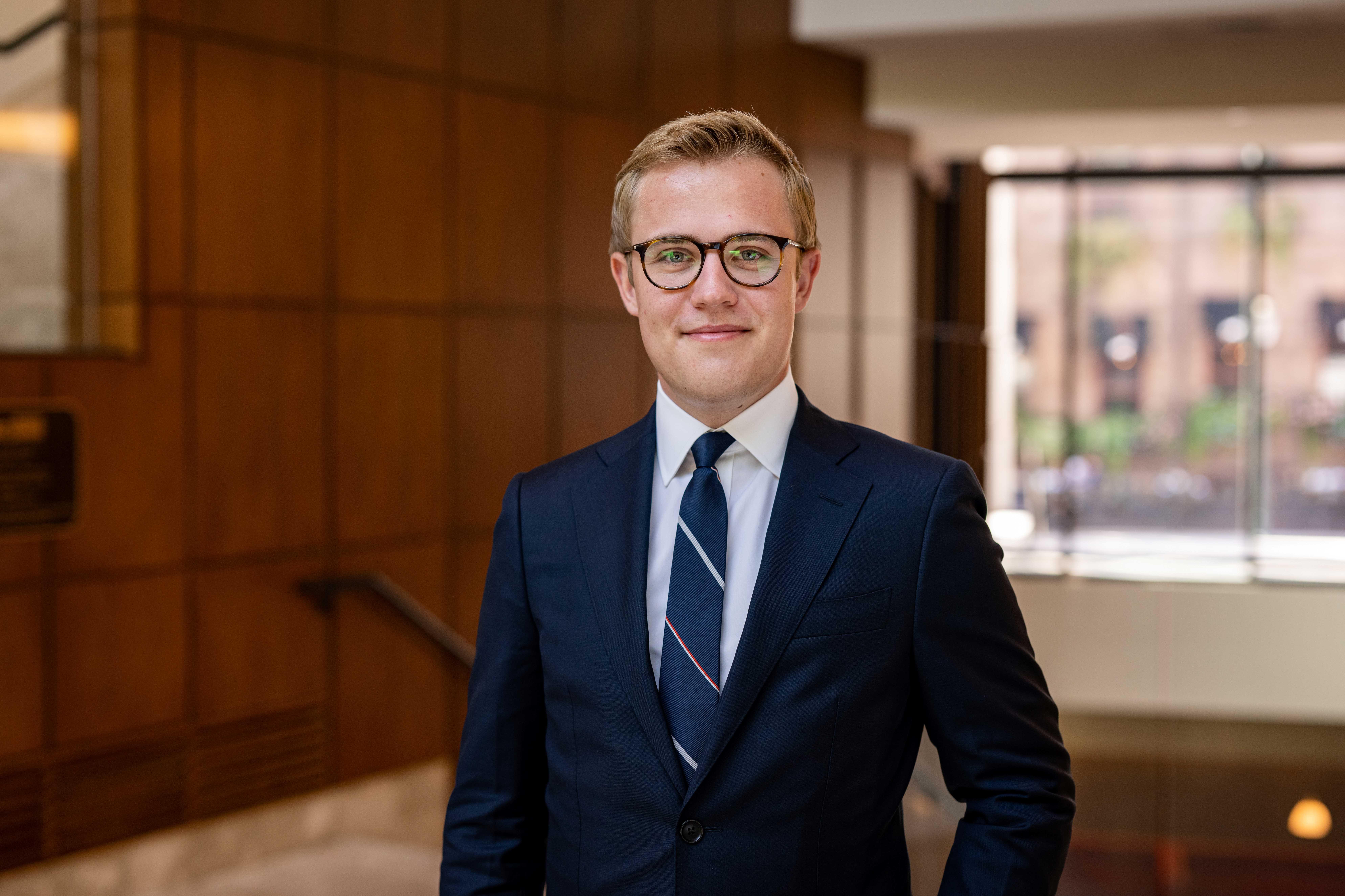 A young white man wearing glasses and in a suit and tie.