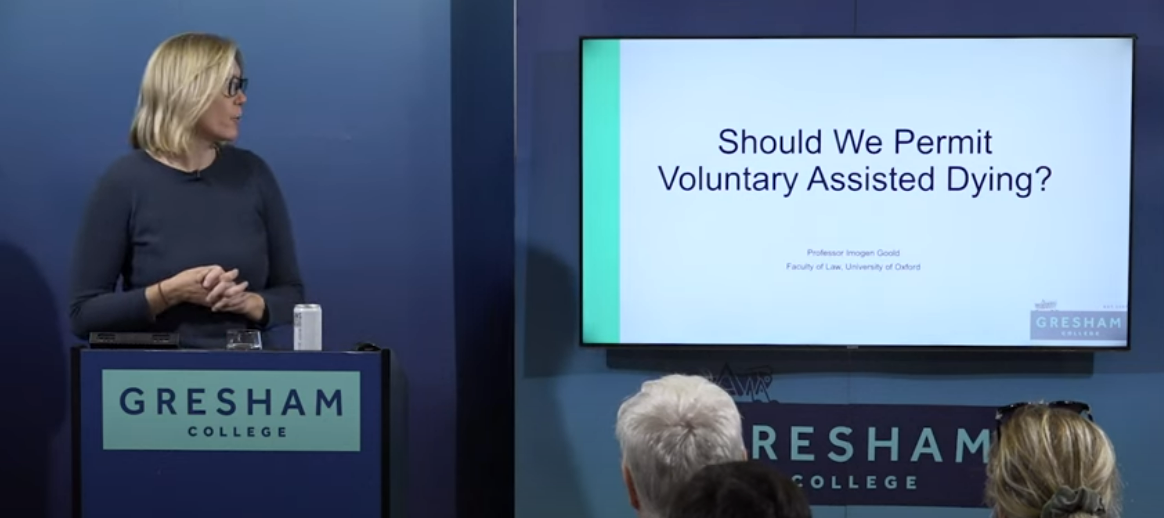 Imogen Goold at a lecturn standing next to screen with title of lecture displayed 