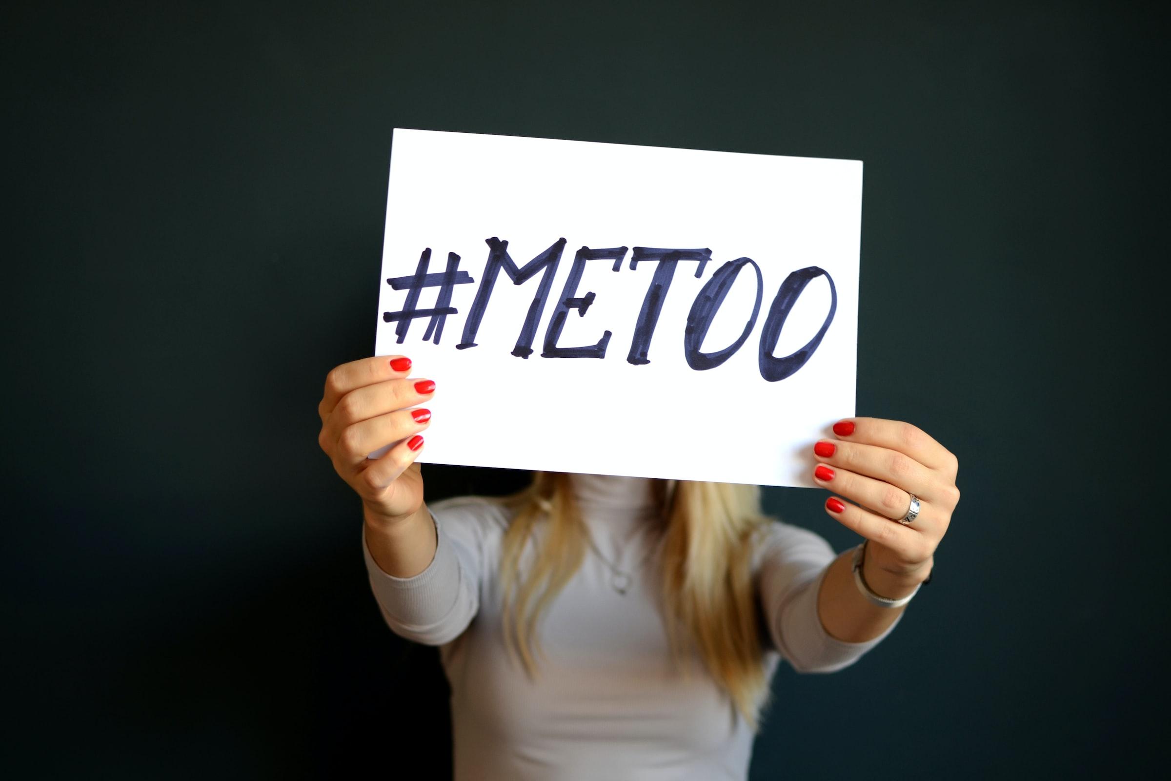 Image of a woman holding up a sign which says #metoo