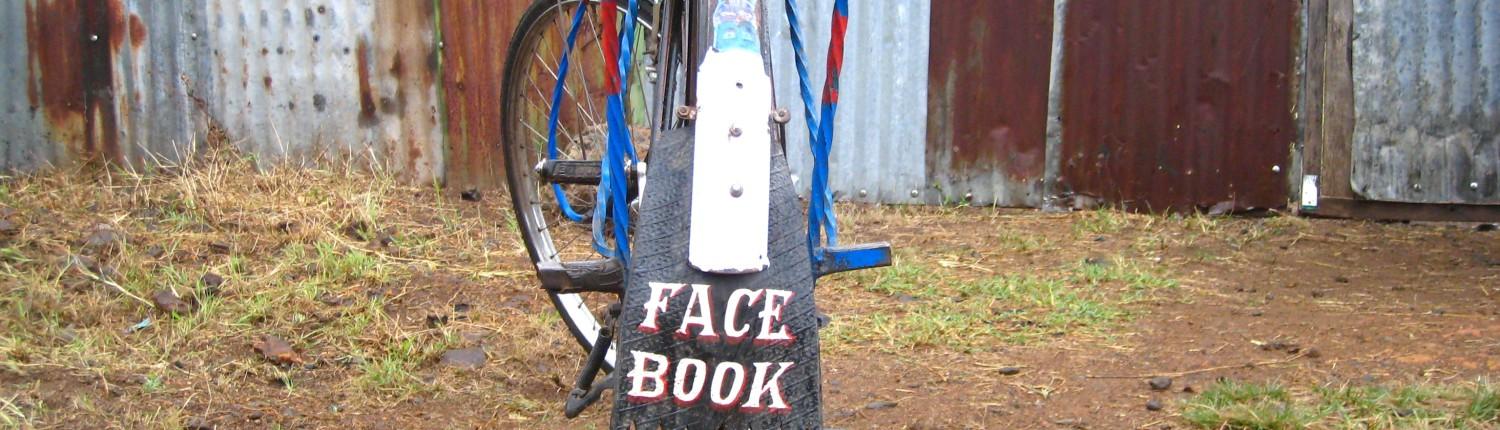 A bicycle with 'Facebook' painted on the mud guard, standing up beside a corrugated fence