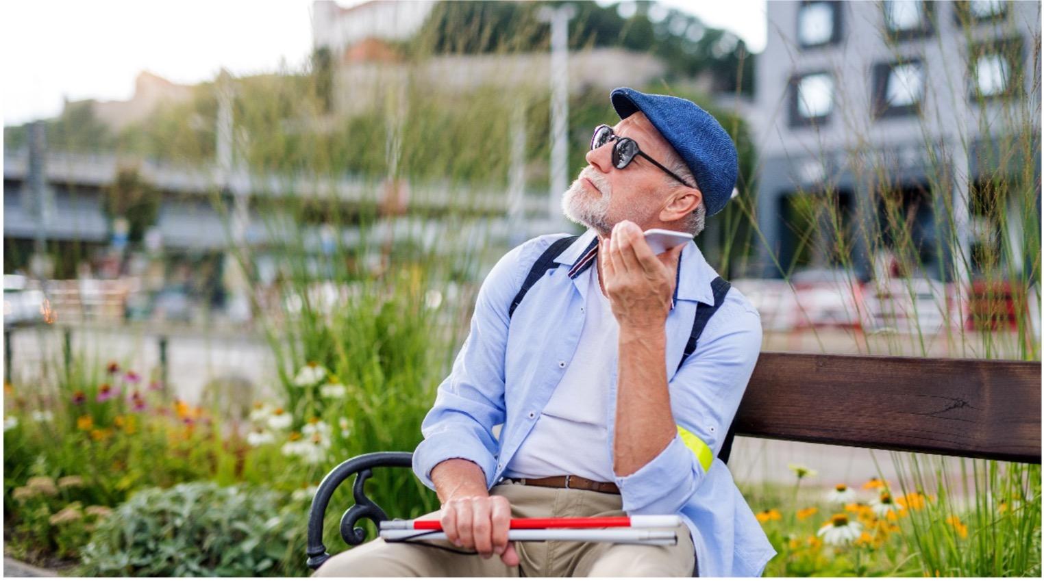 A man with a cane in the park using his phone.