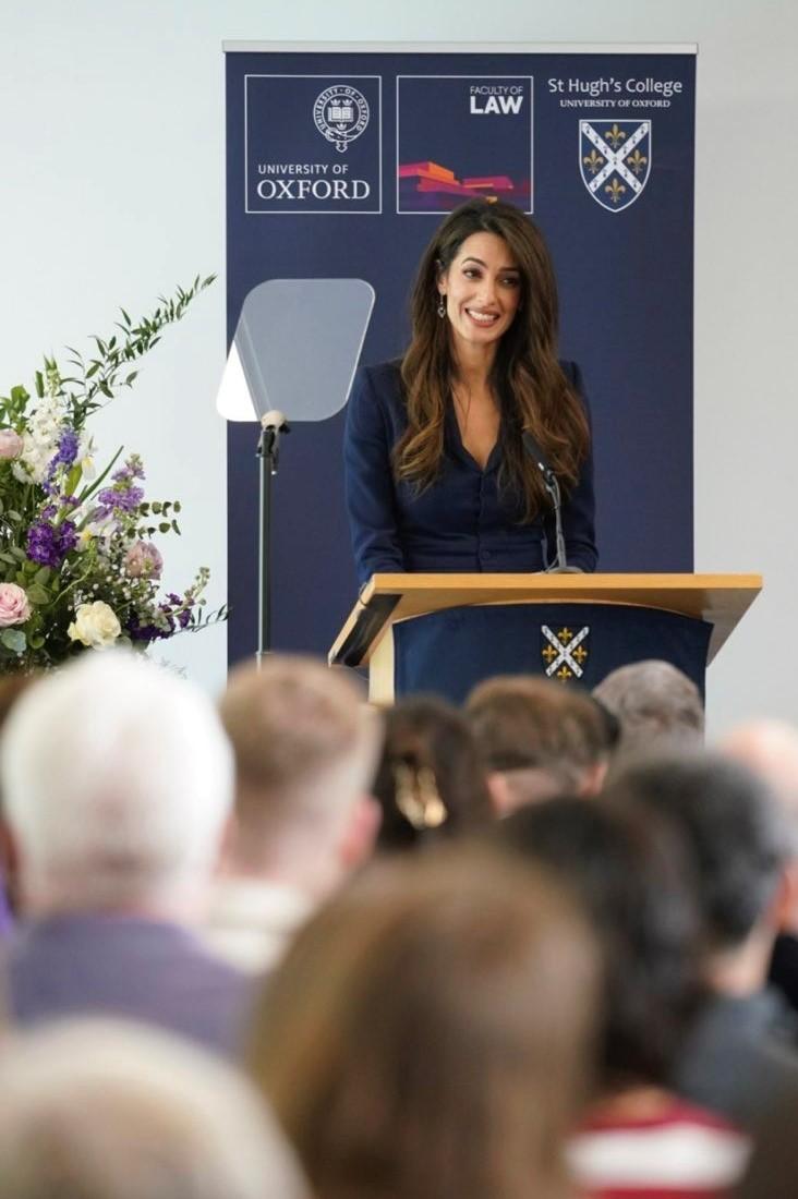 Amal Clooney speaking at a lecturn with audience members in front of her