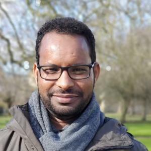 Dr Haleform Abraha, a man with dark hair and glasses and a scarf on a sunny day