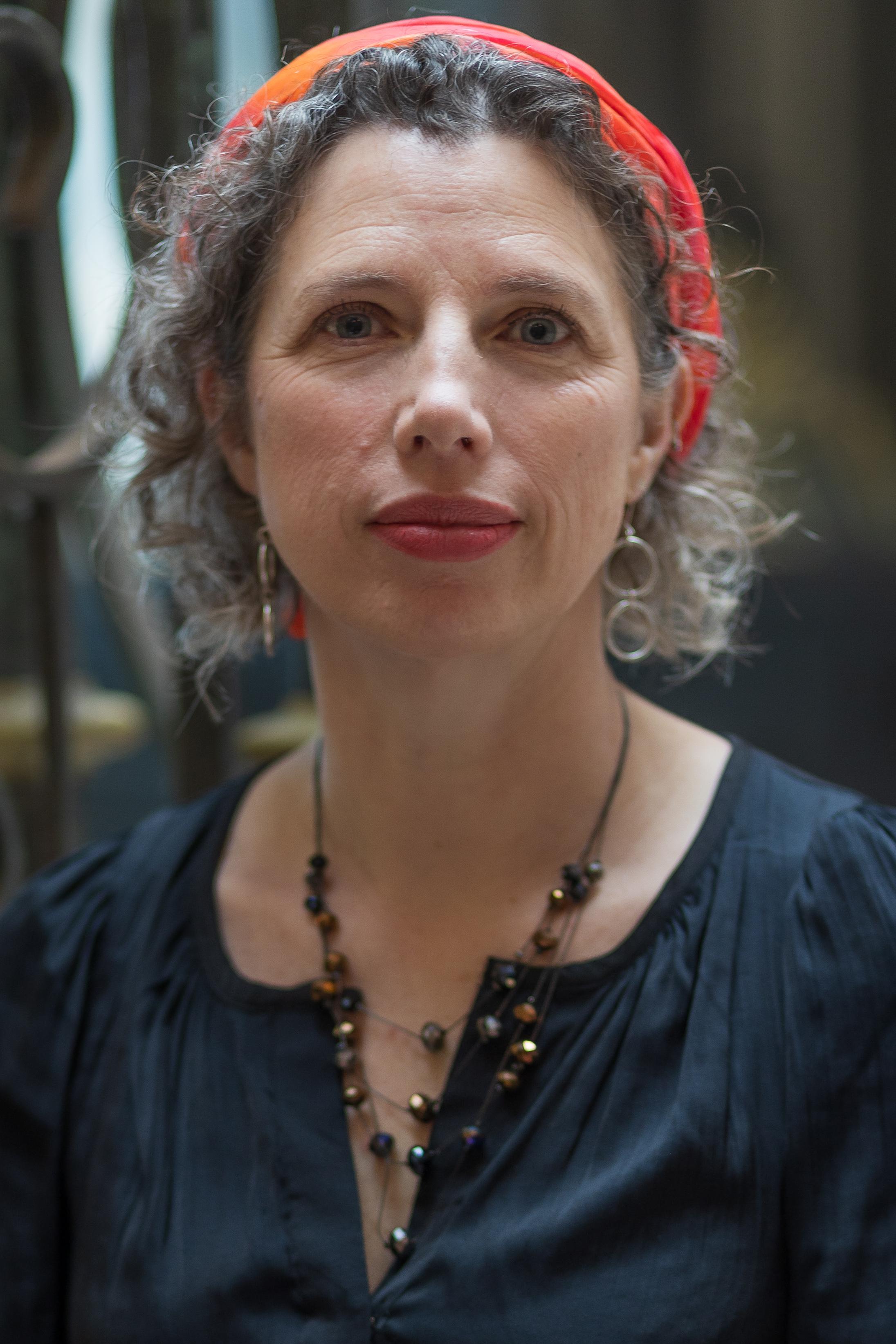 Headshot of white woman with curly grey/brown hair and orange headband
