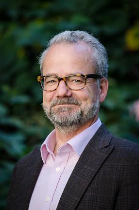 Headshot of a white man with grey hair and beard wearing tortoiseshell rimmed glasses.