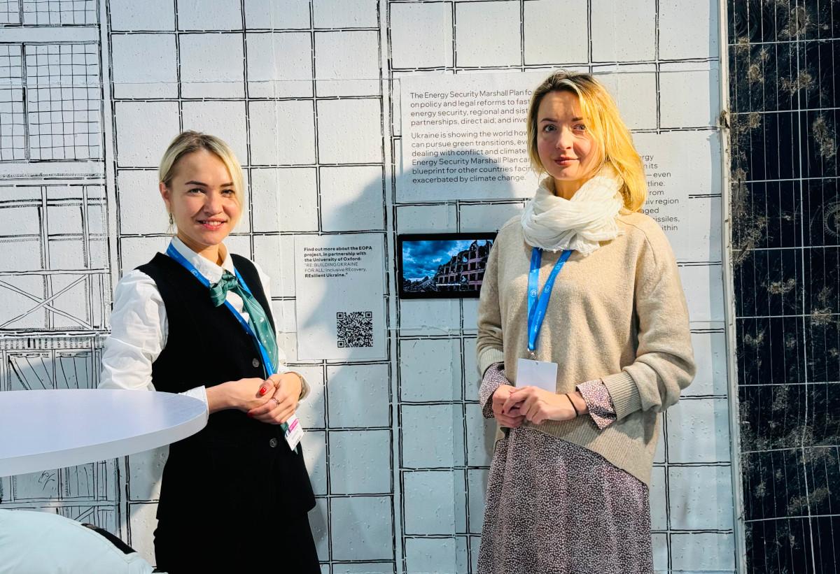 2 women standing in front of display materials on wall 