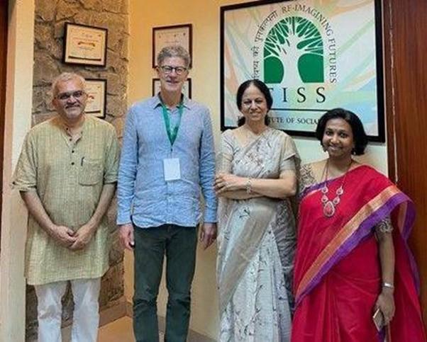Four people standing in a room with a banner showing an outline of a tree in green.  The people are two asian women, one white man and one asian man. They are all smiling.