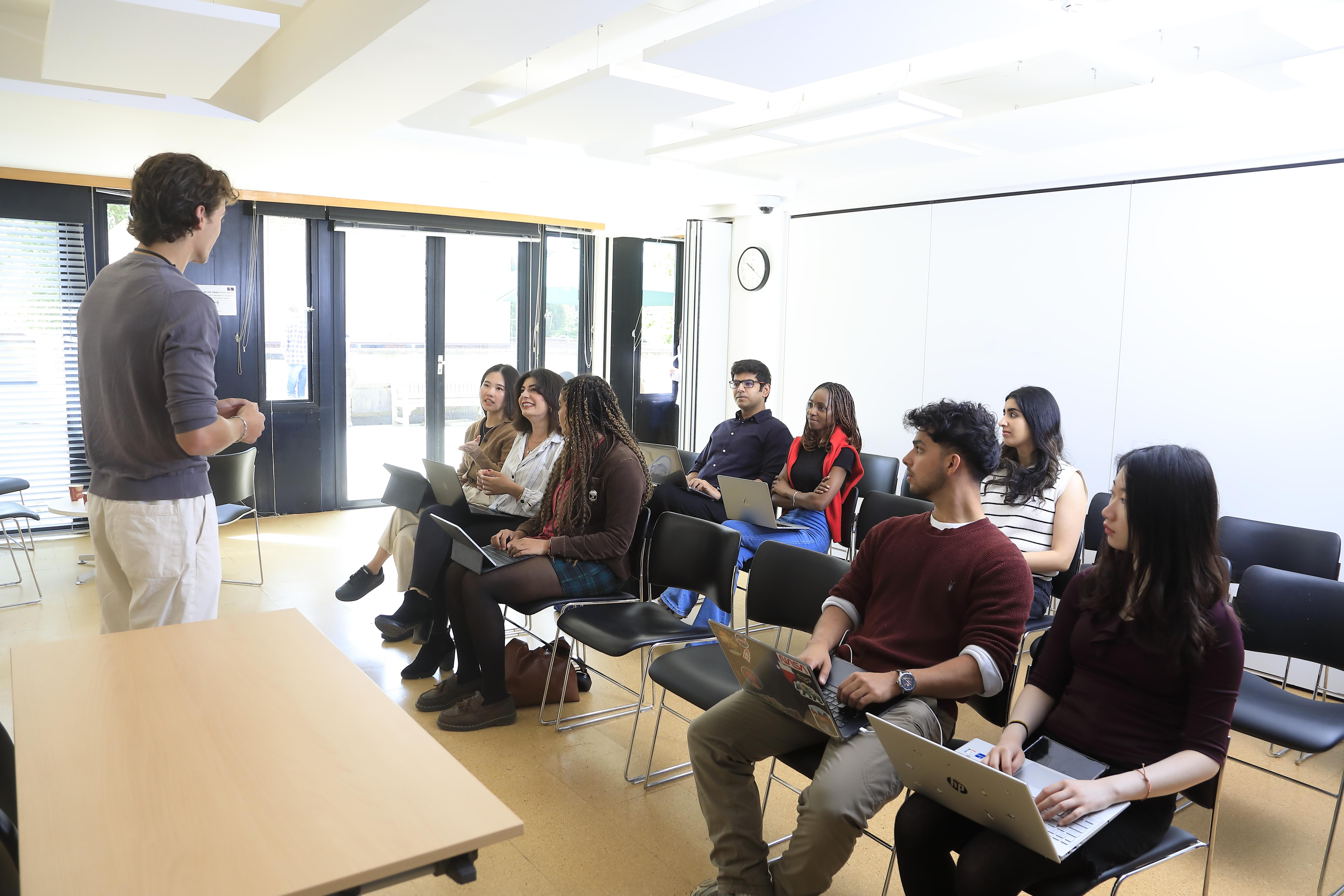 Class being delivered at the Faculty of Law. Students with laptops and desks are facing the speaking teacher.