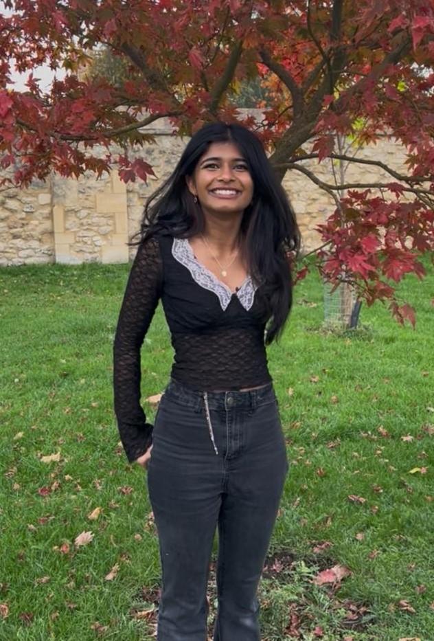 Girl with black hair standing in front of a red tree 