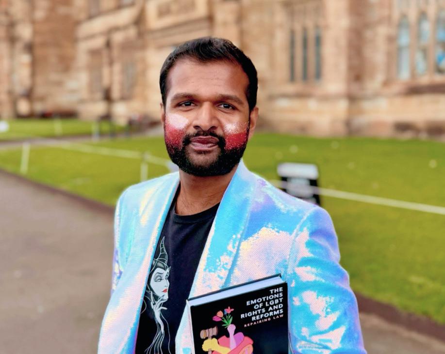 Dr Raj wearing a bright blazer and makeup on his cheek, with the book in hand