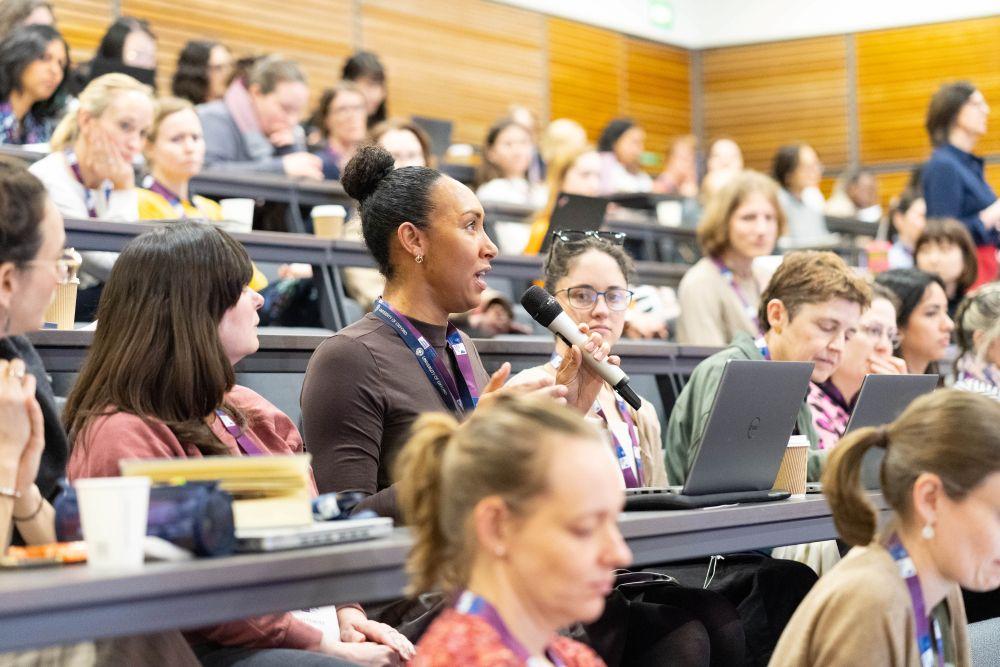 A tiered lecture theatre with an audience of women seated and one woman talking into a microphone.